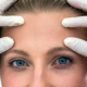 Close-up of a woman’s forehead and eyes with a medical professional’s gloved hands examining her brow area, illustrating an endoscopic brow lift evaluation.