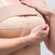 Woman wearing a postoperative compression bra gently supporting her breasts during early breast augmentation recovery.